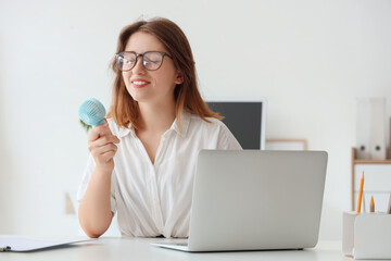 Young woman with small handheld electric fan in office © Pixel-Shot