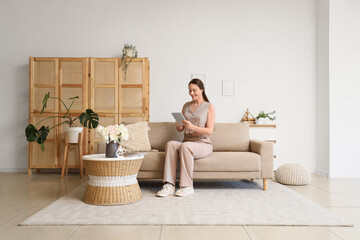 Obraz premium Young woman with tablet computer resting on couch at home
