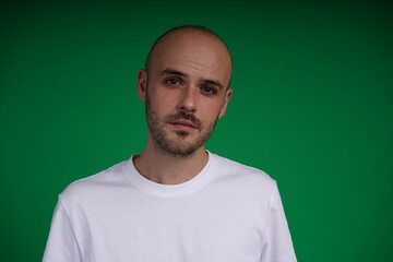 Obraz premium Young man with a variety of emotions, wearing a white t-shirt standing against a green background. Studio shot with copy space.