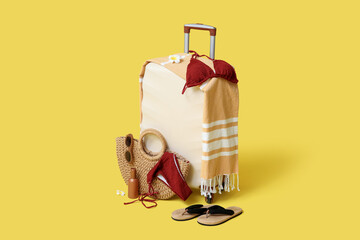 Suitcase, stylish swimsuit and beach accessories on yellow background