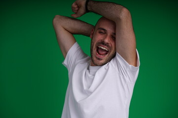 Fototapeta premium Young man with a variety of emotions, wearing a white t-shirt standing against a green background. Studio shot with copy space.