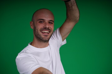 Fototapeta premium Young man with a variety of emotions, wearing a white t-shirt standing against a green background. Studio shot with copy space.