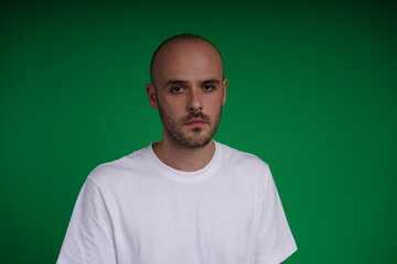 Fototapeta premium young man wearing a white t-shirt standing against a green background. Studio shot with copy space.