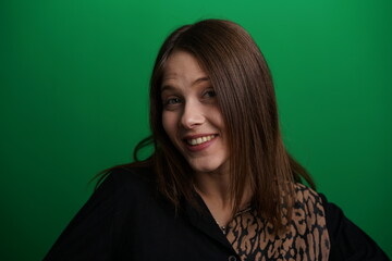 Fototapeta premium A young woman poses in a studio with a green background, showing natural emotions, full of expressions and dynamic movements. Unedited image