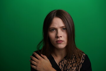 Fototapeta premium A young woman poses in a studio with a green background, showing natural emotions, full of expressions and dynamic movements. Unedited image