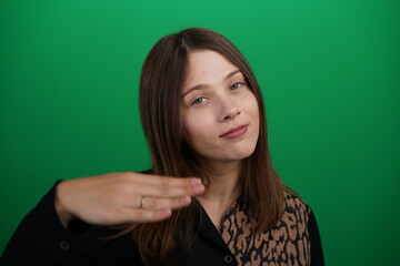 Fototapeta premium A young woman poses in a studio with a green background, showing natural emotions, full of expressions and dynamic movements. Unedited image