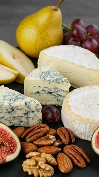 Cheese platter with blue cheese, brie, and camembert. Served with fresh pears, grapes, figs, and assorted nuts on a dark slate board.