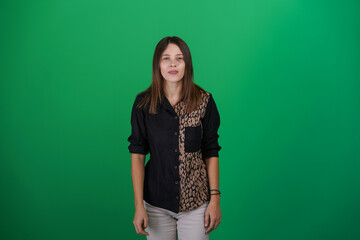 A young woman poses in a studio with a green background, showing natural emotions, full of expressions and dynamic movements. Unedited image