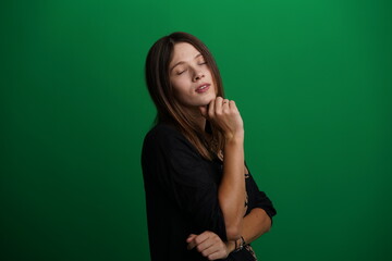 A young woman poses in a studio with a green background, showing natural emotions, full of expressions and dynamic movements. Unedited image