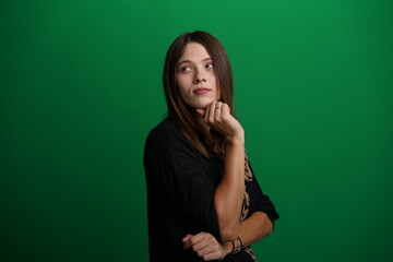 A young woman poses in a studio with a green background, showing natural emotions, full of expressions and dynamic movements. Unedited image