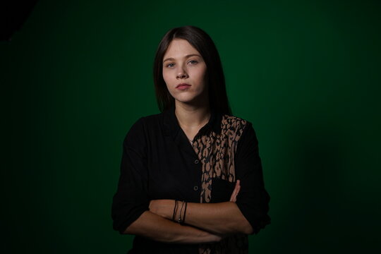 A young woman poses in a studio with a green background, showing natural emotions, full of expressions and dynamic movements. Unedited image