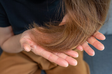 Cropped shot view of Asian woman holding her damaged split ended hair. Hair damage is risk for...