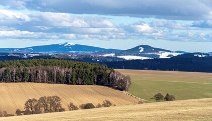 Fototapeta premium Rolling hills, forests, and distant mountains under a partly cloudy sky