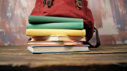 Red Backpack Leaning Against Stacked Books on Rustic Wooden Table with Colorful Background in a Back To School Theme - Powered by Adobe