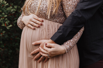 Close-up of pregnant woman in sequined dress with partner's hands embracing her belly, romantic...