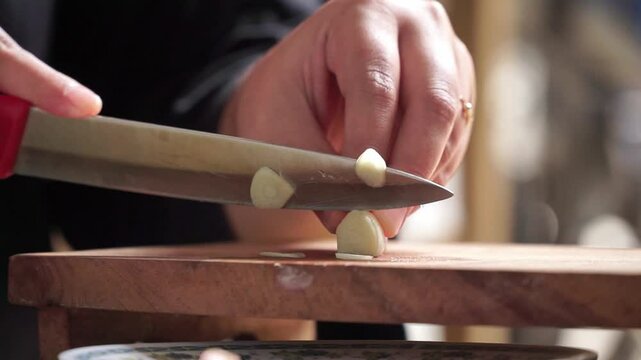 Hands chopping garlic with a knife, a close-up view in a warmly lit kitchen atmosphere.