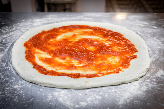 A freshly stretched pizza base, topped with homemade tomato sauce, awaits the ingredients that will complete its flavor.
