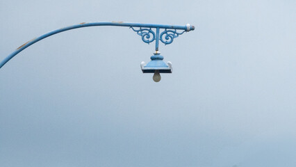 A blue lamppost with intricate details against a soft, light blue background.