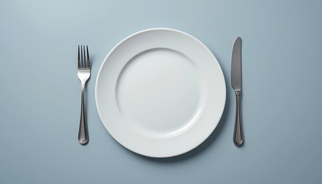 A top down view of a white plate with a fork and knife on a light blue colored surface in a studio - Powered by Adobe