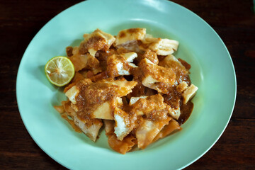 Batagor with Peanut Sauce and Lime. A delicious plate of Indonesian Batagor (fried tofu and fish dumplings), a popular street food from Bandung, generously covered in a rich brown peanut sauce.