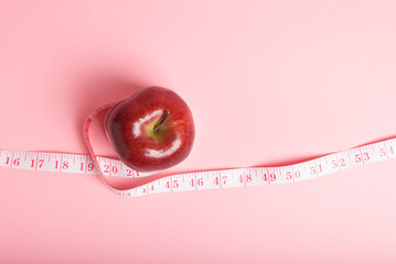 Red apple and a pink measuring tape on a pink background, healthy eating and weight management.