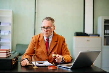 Senior male judge reading documents with gavel in hand at desk. Legal justice concept with law...