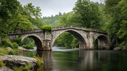 Fototapeta premium Historic stone bridge spanning a tranquil river, surrounded by green foliage