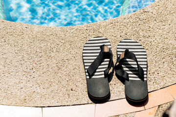Black striped flip flops placed by the pool edge in sunlight