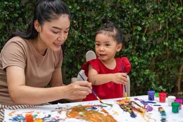 happy mother and toddler girl painting watercolor in paper at backyard.