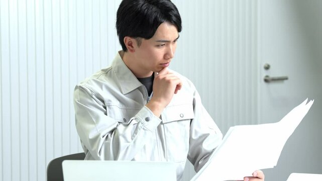 ノートパソコンを前に図面を見る作業着を着た男性