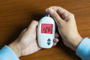 Woman's hands checking diabetes and hyperglycemia with digital blood sugar meter. Healthcare and...