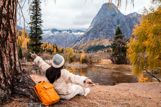 Young female tourist relaxing and enjoying at beautiful autumn scenery landscape at Mount Siguniang national park in Sichuan, China