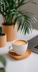 Latte art on a white mug, plants, and a laptop