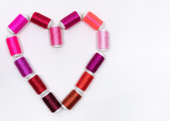 Obraz premium Heart Made of Pink and Red Thread Spools with Copy Space on Light Background