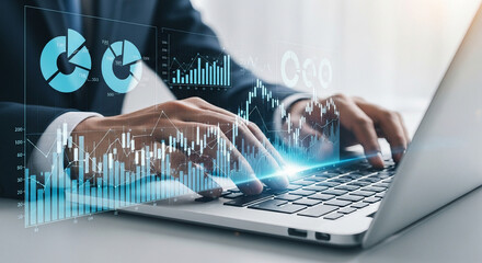 Hands typing on laptop with holographic financial charts and data visualizations overlay