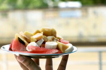 A man hand holding plate of fresh fruit salad