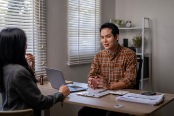A man and a woman are sitting at a desk, talking to each other