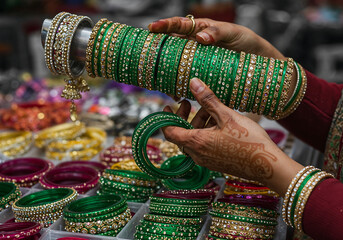 Woman’s Hands Sorting Sparkling Green Glass Bangles at Festive Market Stall with Henna