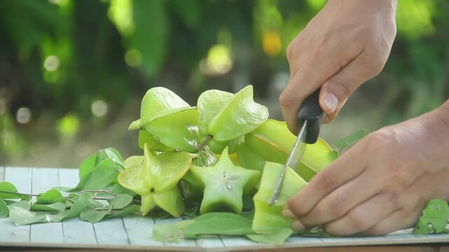 A man slicing fresh Averrhoa carambola or star fruit arranged on an outdoor table