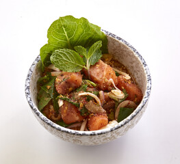 Bowl of spicy salmon salad garnished with fresh mint leaves, lettuce, and sliced onions, served...