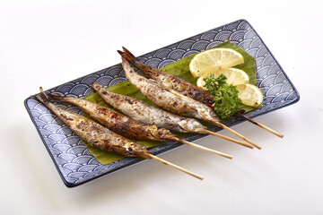 Grilled shishamo fish skewers served on decorative plate with lemon slices and parsley garnish, showcasing traditional Japanese dish