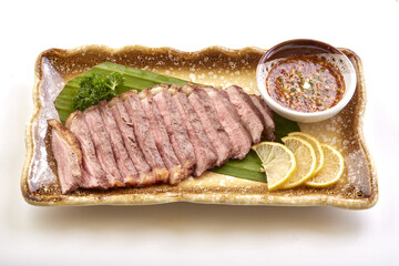 Grilled beef slices served on ceramic plate with side of spicy dipping sauce, garnished with lemon slices, parsley, and presented on banana leaf for appetizing presentation