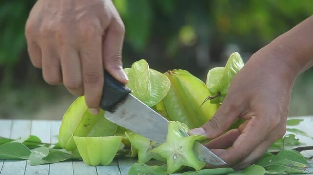 A man slicing fresh Averrhoa carambola or star fruit arranged on an outdoor table