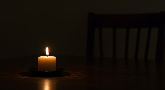 A single lit candle illuminates a dark room, casting shadows on a wooden table.