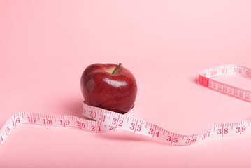 Red apple and a pink measuring tape on a pink background, healthy eating and weight management.