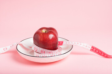 Red apple and a pink measuring tape on a pink background, healthy eating and weight management.