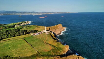 A stunning aerial view of a lighthouse by the coast, surrounded by a lush green landscape and...