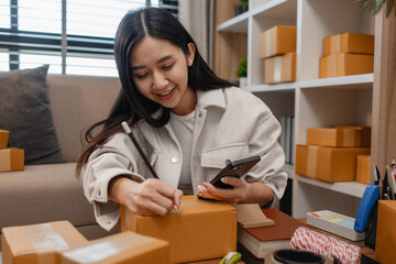an entrepreneur is packing parcel for order from customer, she own a small business, sme, a lot of package in the room, e-business is running by a this entrepreneur, online shopping