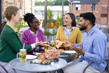 Group of friends enjoy pizza and drinks at an outdoor restaurant, laughing and talking.