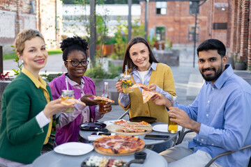 A diverse group of friends enjoying pizza and drinks together outdoors on a patio, smiling and having fun.